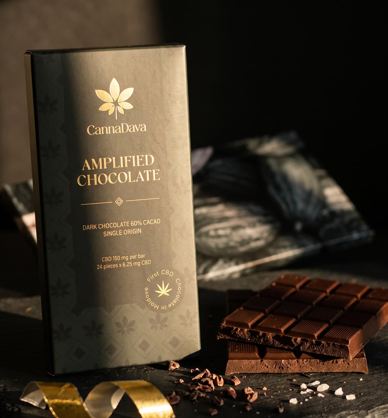 Tableta Amplified Chocolate pe o lespede de ardezie, alături de pătrate rupte de ciocolată, boabe de cacao sfărâmate și fulgi de sare